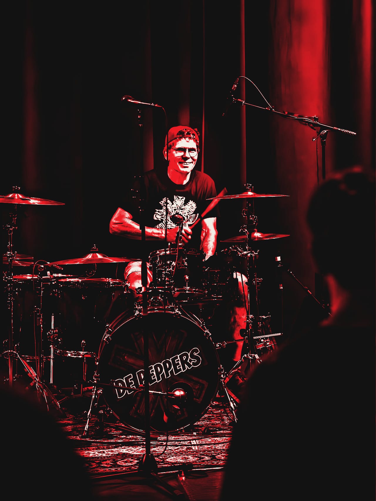 Jan, drummer van De Peppers, lacht achter zijn rode drumstel met het De Peppers-logo op de bassdrum